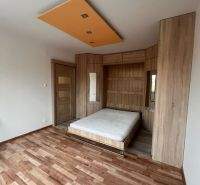 A one-room apartment with a wooden decor floor, a bed, and wooden cabinets.