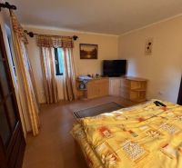 Bedroom in a family house with a bed, dresser, and television, floor with wooden decor.