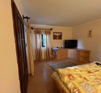 Bedroom in a family house with a television, dresser, and bed, floor with a wooden decor.