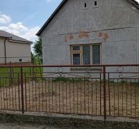 A family house in Ňárad with worn-out plaster and an iron fence, blue sky.