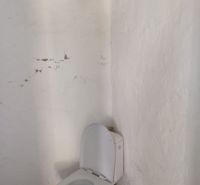 A bathroom in a family house with a white toilet and cracked plaster on the walls.