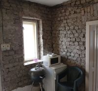 A room with brick walls, a grill, a microwave, and a plastic chair in a family house.