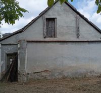 A family house in Ňárad with peeling plaster and a closed attic window, surrounded by greenery.