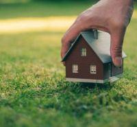 A hand places a small wooden house on the lawn in the gardens of Dunajská Streda.