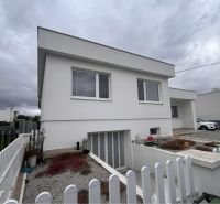 A family house in Trstice with a white facade and a white fence under a cloudy sky.