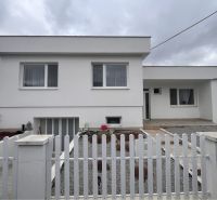 A family house in Trstice with a front garden, a white fence, and a gray-white facade.