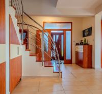 A hallway in a family house with wooden decor on furniture, stairs, and glass doors.