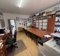 An office with wooden floor decor, a large desk, shelves full of documents, and a computer.