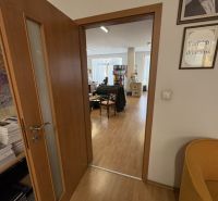 An interior with wood-patterned flooring and open doors leading to an office.