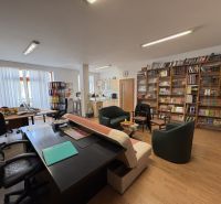 An office with a lot of books, tables, and a wooden decor floor in a 3-room apartment.