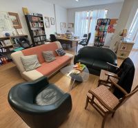 Interior of an office with wood-patterned flooring, sofas, and books.