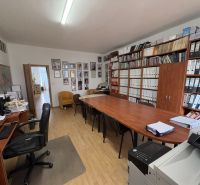 An office with a wood-patterned floor, a desk, chairs, and shelves full of binders.