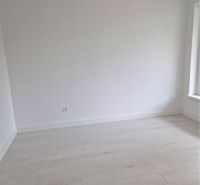 An empty room with white walls and a wooden decor floor in a 3-room apartment.
