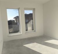 A room in a family house with a bare floor and large windows, light streaming in.