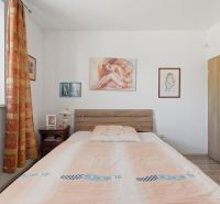 Bedroom in a family house with paintings, a bed, and a nightstand, floor with wooden decor.
