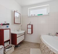 Bathroom in a family house with a bathtub, sink, cabinets, and a window.
