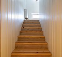 A staircase with a wooden decor and walls in white shades in a family house.