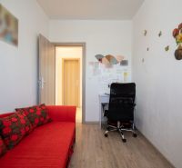 A room in a family house with a red sofa, a desk, and a wooden-patterned floor.