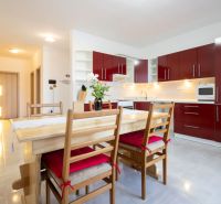 A kitchen in a family house with red cabinets, a dining table, and a light floor.