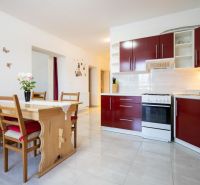 A kitchen in a family house with red cabinets and a wooden dining table.