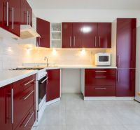 A kitchen with red cabinets in a family house, white appliances, light tiles.