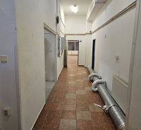A corridor with light walls, tiles, and piping in commercial premises.