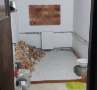 A room in a family house with tiles, stored building materials, and a radiator.