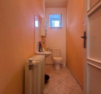 A toilet in a family house with a radiator, a sink, and a small window.