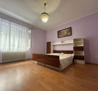 A room in a family house with a bed, purple walls, and a wood-patterned floor.