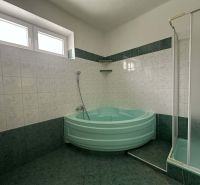 A bathroom in a family house with a corner bathtub and a shower, green tiles.