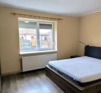 Bedroom in a family house with a wood-patterned floor and a large window.
