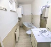 A bathroom in a family house with a bathtub, sink, and radiator, with light wall tiles.