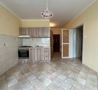 A kitchen in a studio apartment with a tiled floor and light-colored furniture.