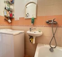 A bathroom in a studio apartment with a bathtub, washing machine, and small sink.