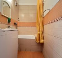 Bathroom with a bathtub and a washing machine in a studio apartment with orange tiles.