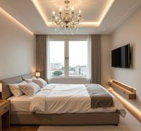 A bedroom in a studio apartment with a chandelier, a bed, and a TV on the wall.