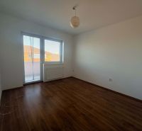 A room in a three-room apartment with a wood-patterned floor and a large window.