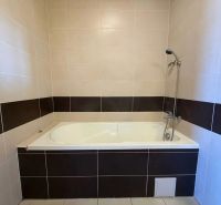 A bathroom with a built-in bathtub and patterned tiling in a three-room apartment.