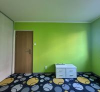 A room in a 3-room apartment with a green wall, a cabinet, and a colorful carpet.