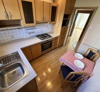 A kitchen in a 3-room apartment with a stove, sink, table, and a floor with a wooden decor.