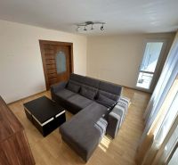 A bright living room with a corner sofa and a wooden decor floor in a 3-room apartment.