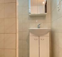 Bathroom in a studio apartment with a sink, mirror, and light tiles.