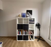 Bookshelf with books and decorations, fan, wooden decor floor, studio apartment.