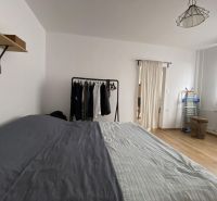 A bedroom in a studio apartment with a bed, a clothes rack, and a wooden decor floor.