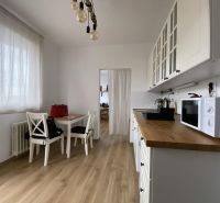 White kitchen with wood-patterned flooring, table, and chairs in a studio apartment.