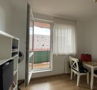 A one-room apartment with a wooden decor floor, a table, chairs, and a shelf by the window.
