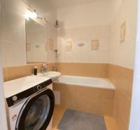 Bathroom with a bathtub and a washing machine in a studio apartment, light tiles and a mirror.