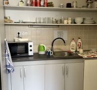 Kitchenette in commercial premises with a microwave, dishes, and shelves with drinks.