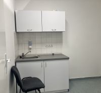 A sink with a white cabinet and a chair in commercial premises.