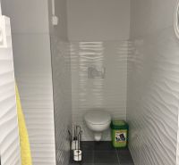Bathroom with toilet, tiled floor, and white embossed walls.
